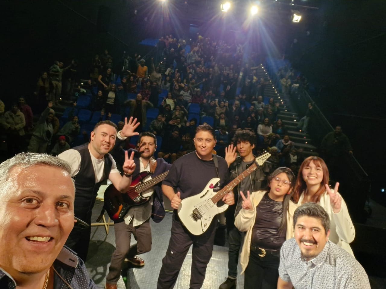 Selfie de la banda en el escenario con el teatro lleno detrás